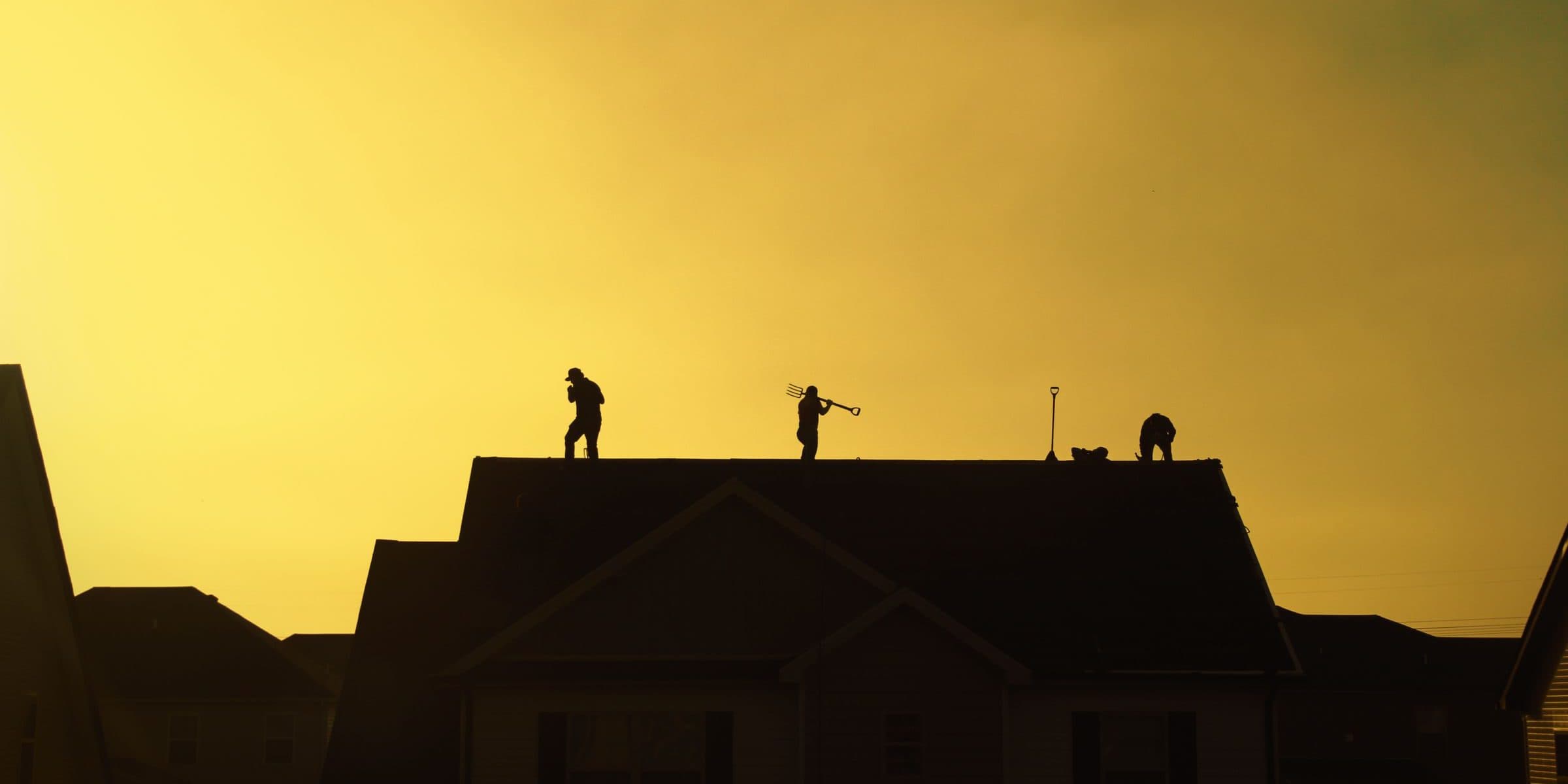 Three roofers silhouetted on a ridge against a sunset